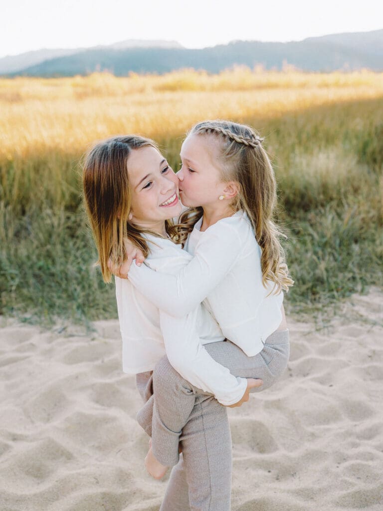 Two little girls dressed in white shirts stand on the beach, part of a family photo session in South Lake Tahoe.