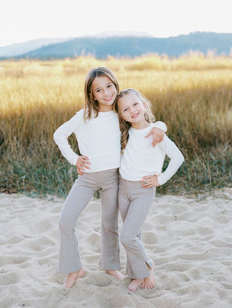 Two little girls dressed in white shirts poses on the beach, part of a family photo session in South Lake Tahoe.