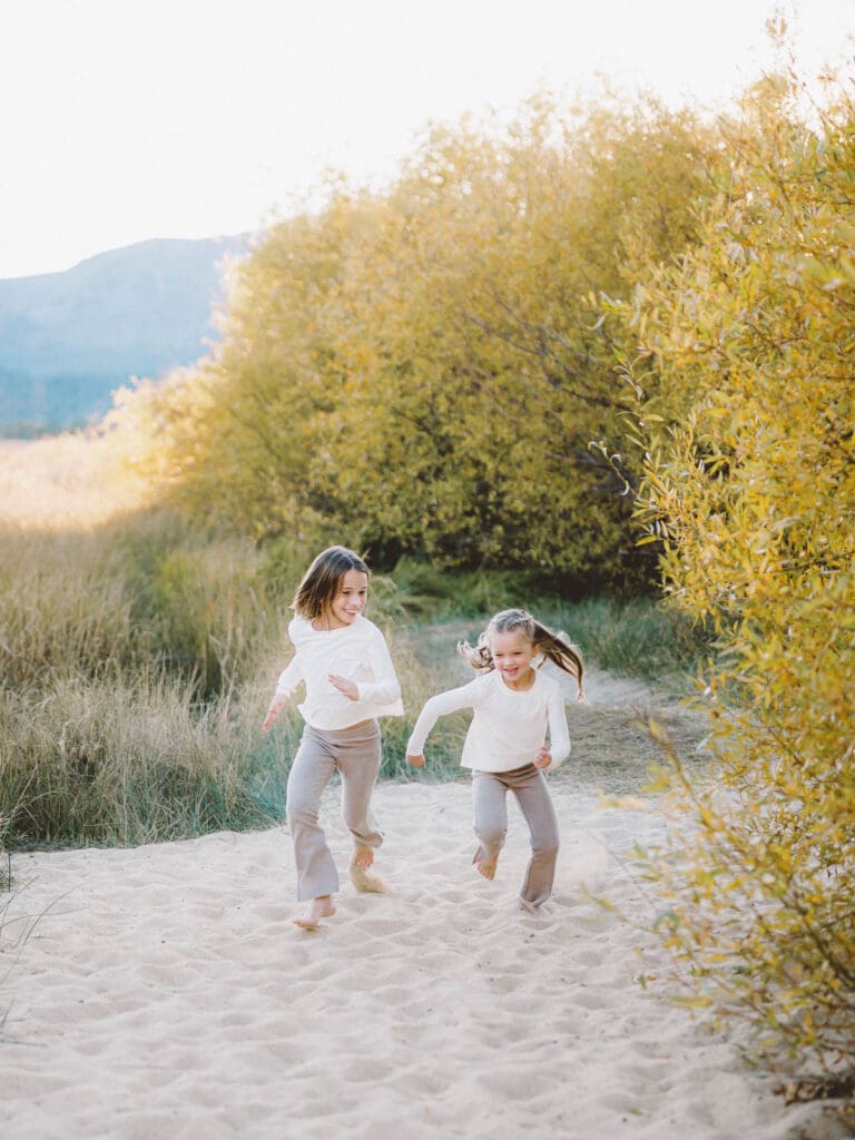 Two little girls dressed in white shirts running on the beach, part of a family photo session in South Lake Tahoe.