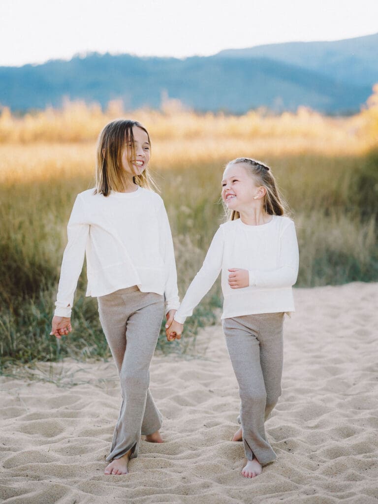 Two little girls dressed in white shirts walking on the beach, part of a family photo session in South Lake Tahoe.