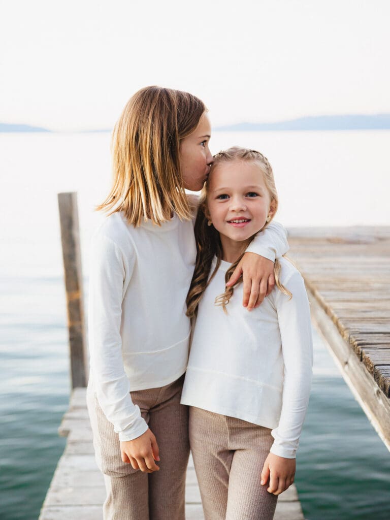 Two little girls dressed in white shirts posing on the dock, part of a family photo session in South Lake Tahoe.