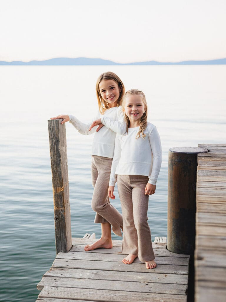 Two little girls dressed in white shirts posing on the dock, part of a family photo session in South Lake Tahoe.