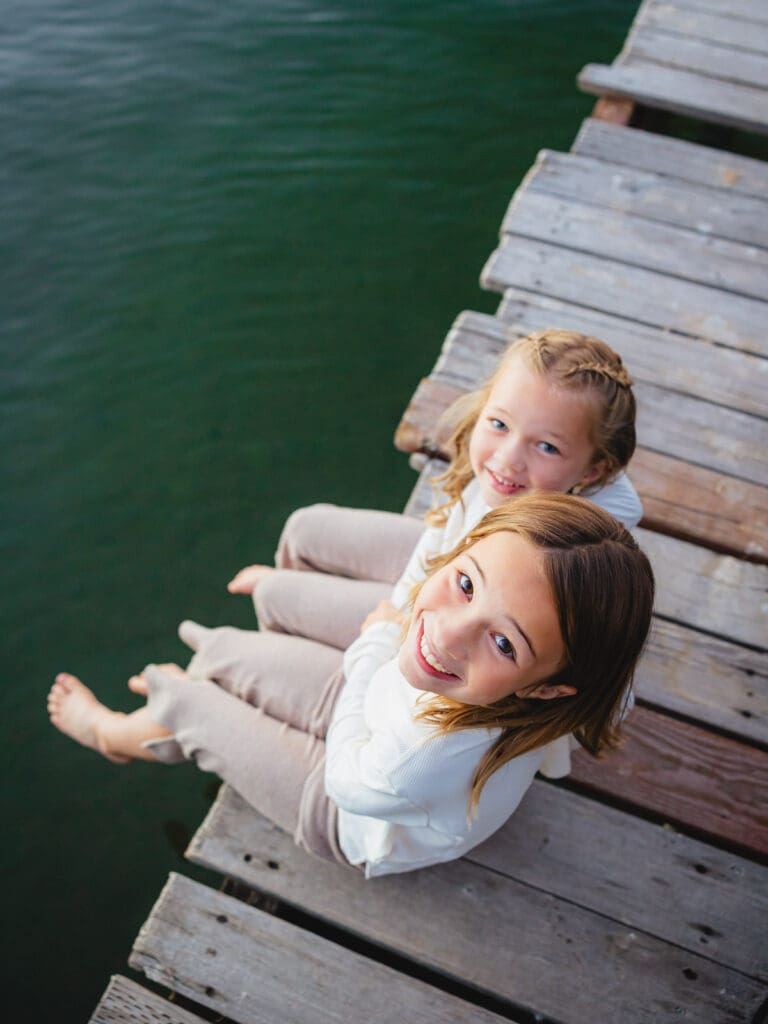 Two little girls dressed in white shirts sitting on the dock, part of a family photo session in South Lake Tahoe.