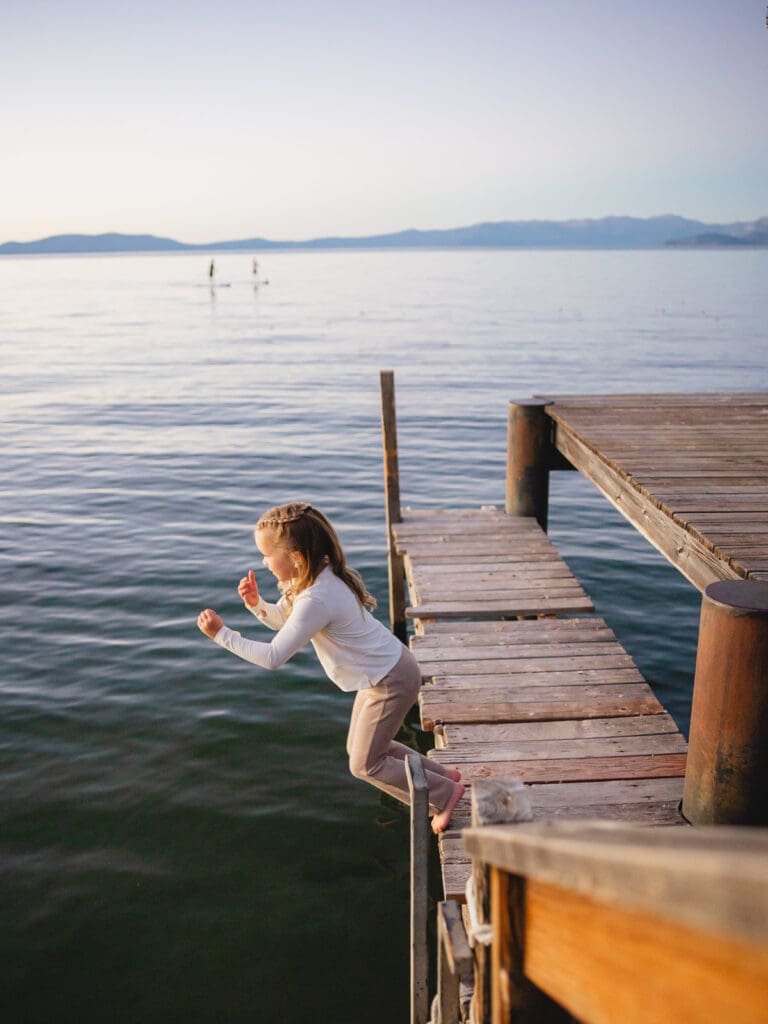 A little girl dressed in white shirts jumping off the dock, part of a family photo session in South Lake Tahoe.