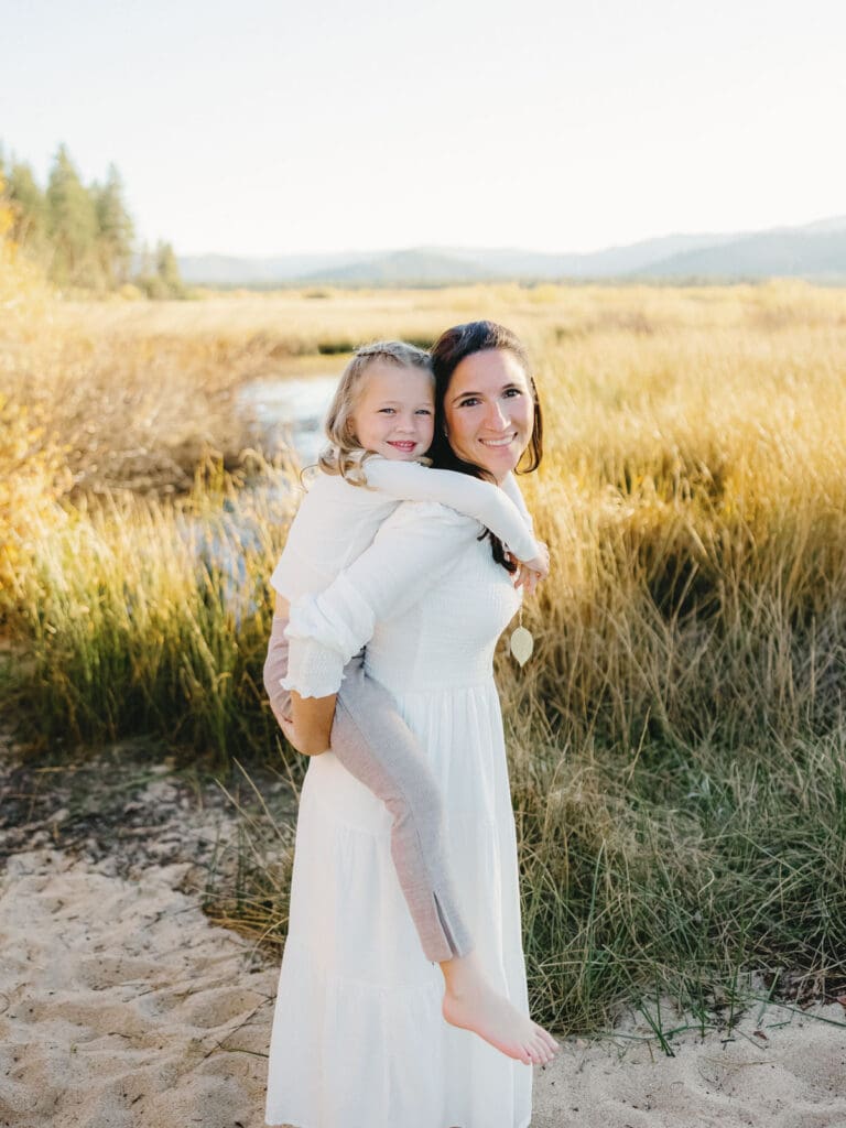 A family photo session at South Lake Tahoe features a mother and her daughter in white dresses standing on the sandy shore.