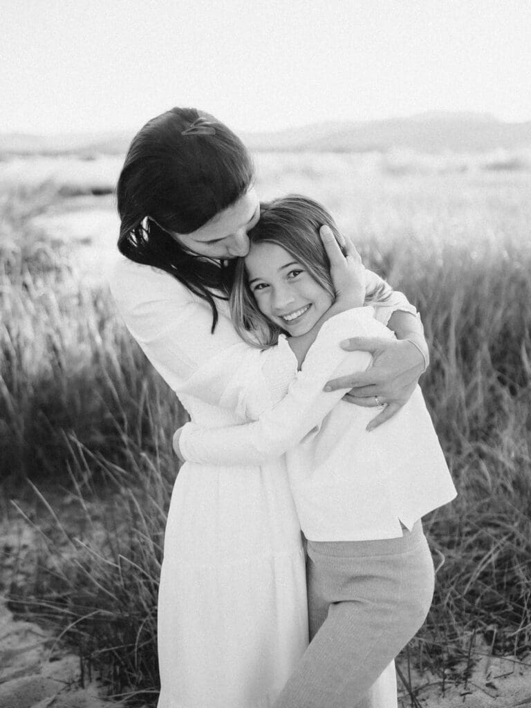 A family photo session at South Lake Tahoe features a mother and her daughter in white dresses standing on the sandy shore.