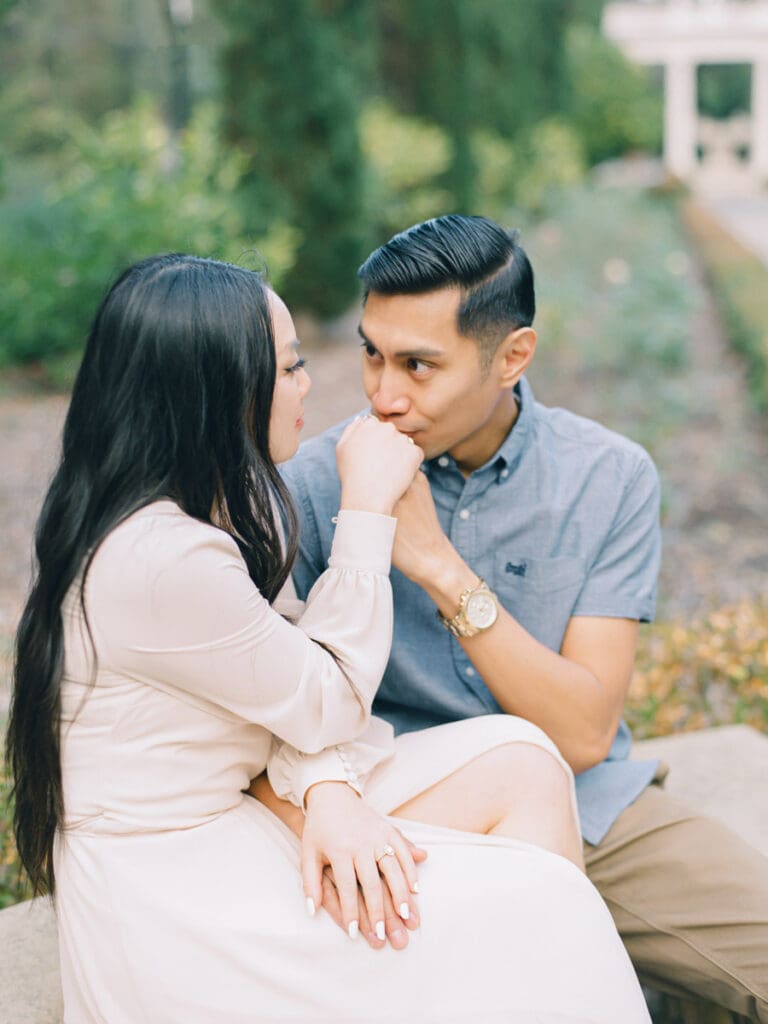 He kisses her hand at romantic Villa Montalvo engagement session in San Francisco, showcasing a couple's love amidst stunning landscapes.